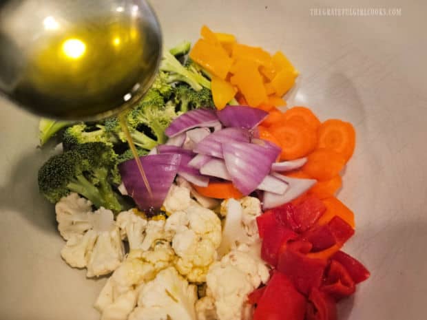 Chopped raw veggies are drizzled with olive oil before adding spices.