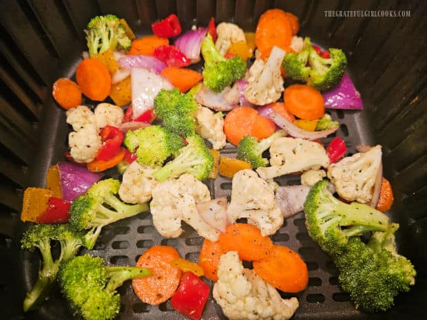 Seasoned veggies are spread in a single layer in the air fryer basket for cooking.