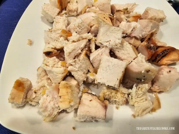 A large, cooked chicken breast is cut into small cubes before it's added to hot pasta.