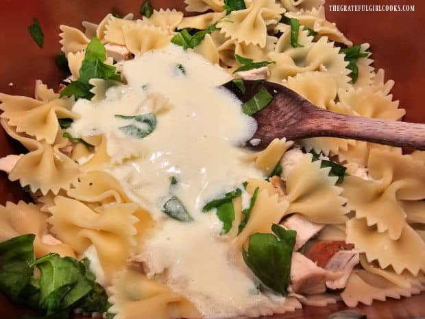 Hot alfredo sauce is added to the pasta, chicken and spinach in the saucepan.