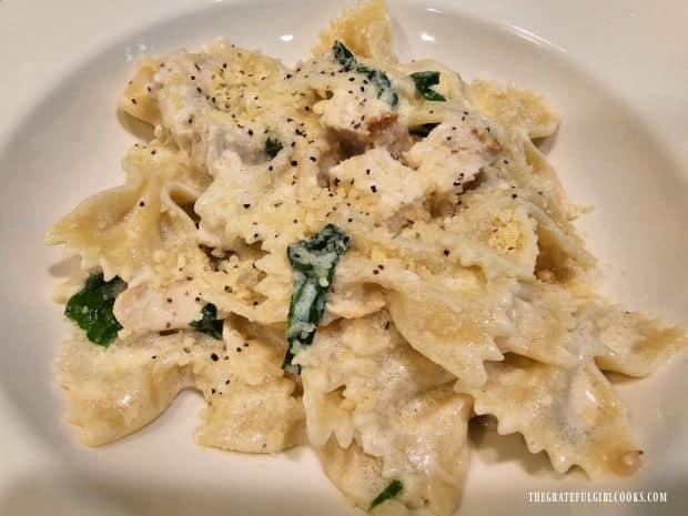 A bowl of bowtie pasta alfredo and chicken is served, topped with Parmesan cheese and pepper.