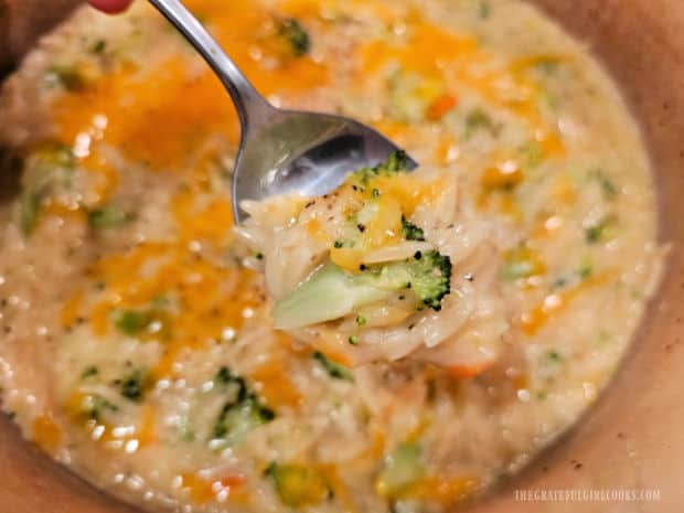 A spoonful of the creamy broccoli cheese orzo is shown over the pan.