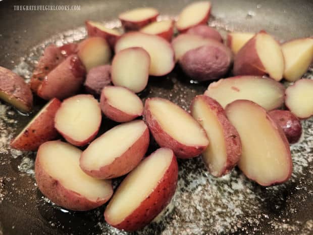 Red potatoes are boiled in water until tender, then halved and cooked in butter and garlic.