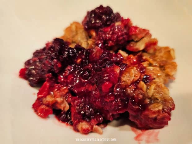 A portion of warm blackberry crisp is placed in a serving bowl.