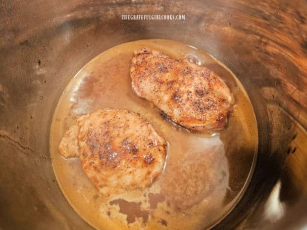 The browned pork chops are added back into the sauce in the Instant Pot.