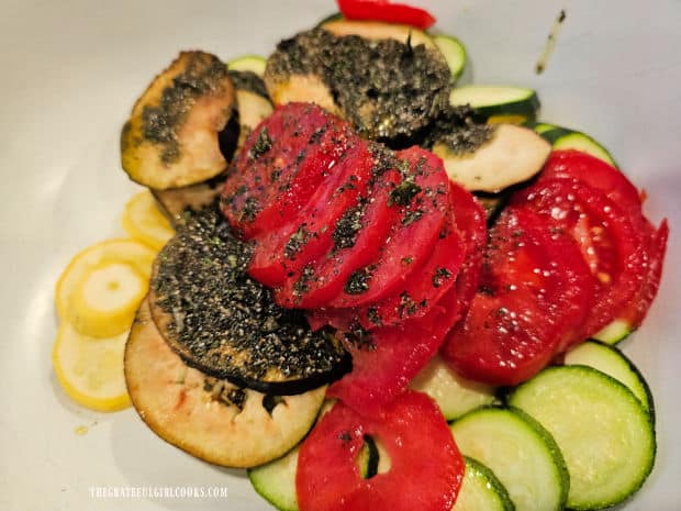 The oil and spices are added to the bowl of sliced veggies.