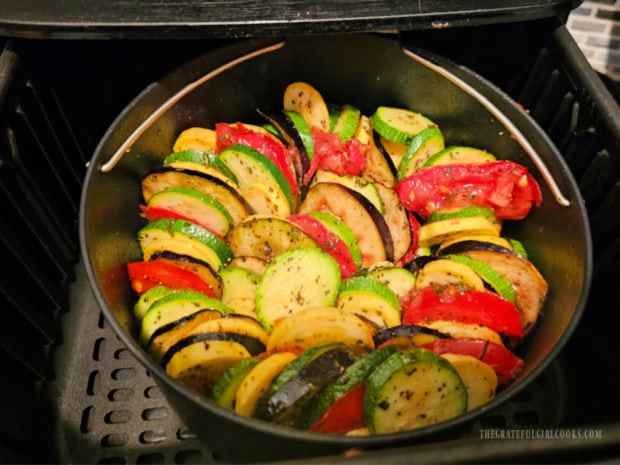 The sliced veggies are layered, alternating colors on top of the onions/garlic in pan.