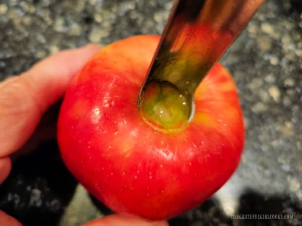 An apple corer is inserted in apple to remove seeds and middle core.