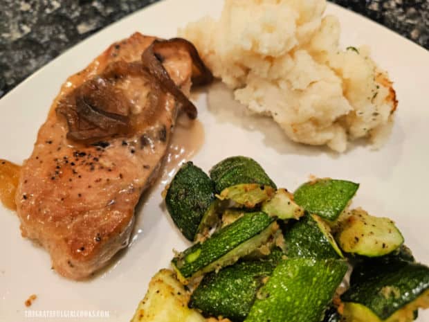 A pork chop placed on plate with mashed potatoes and zucchini.