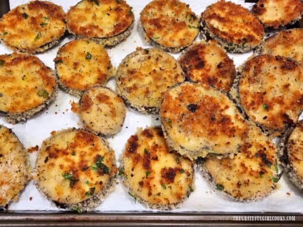 Cooked eggplant slices drain on paper towel-lined baking sheet.