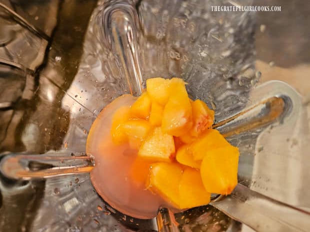 Looking down into a blender of pink lemonade and chopped peaches.