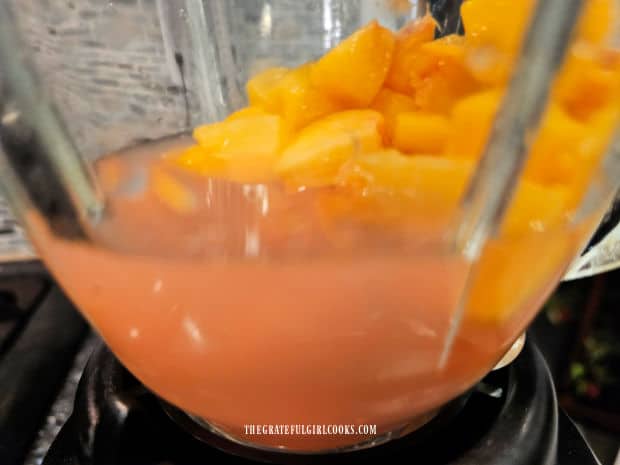 A side view of pink lemonade and chopped peaches in a blender before mixing.