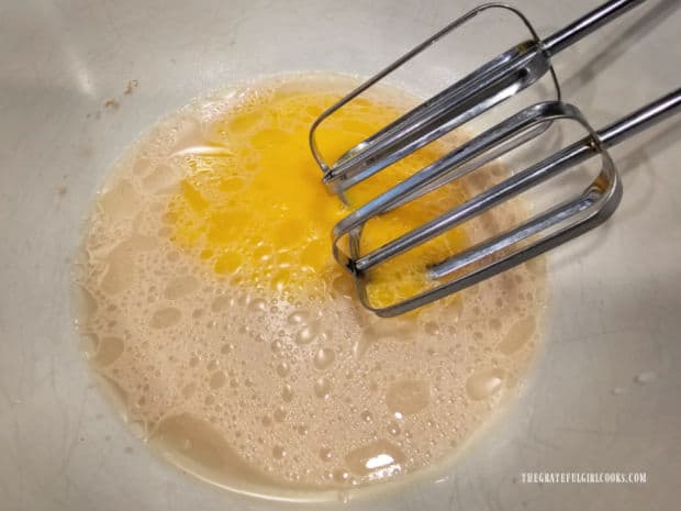 Three egg yolks are beaten into the yeast mixture in a bowl.