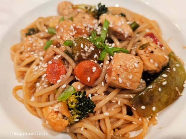 Asian Chicken Pasta Stir-Fry is served, garnished with green onions and sesame seeds.
