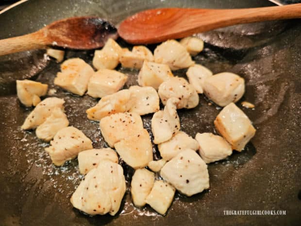 A large chicken breast is cut in chunks and sautéed in a skillet.