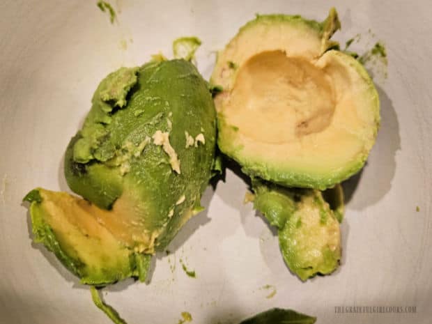 A ripe avocado is peeled and pitted, then placed in a bowl for mashing.