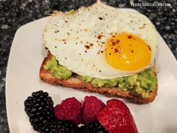 A fried egg (over medium) is added on top of the mashed avocado toast.