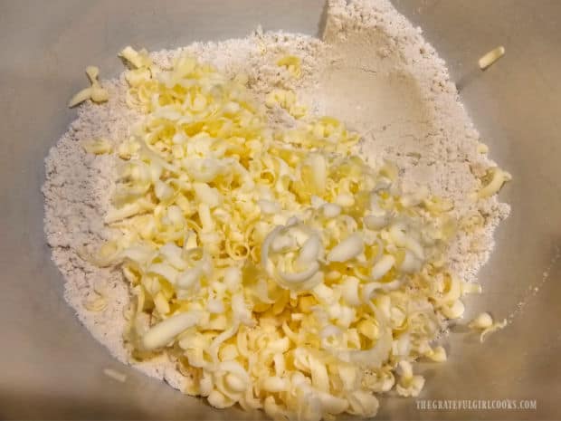 Cold grated butter is added to Bisquick mix and baking powder in a bowl.