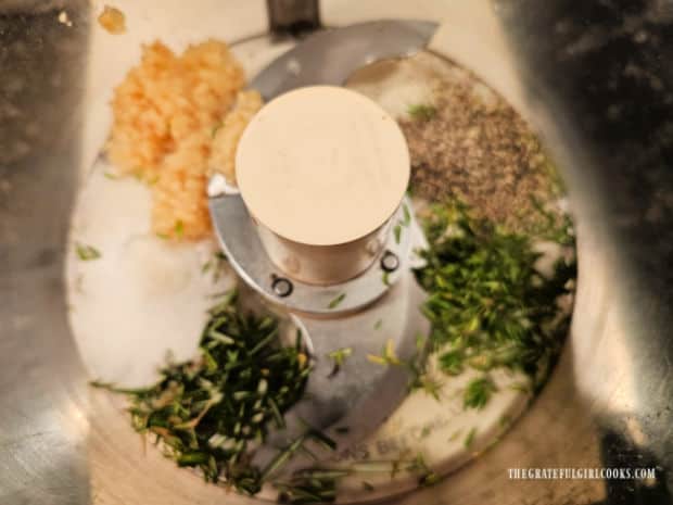 Fresh herbs and minced garlic cloves are finely chopped in a food processor.