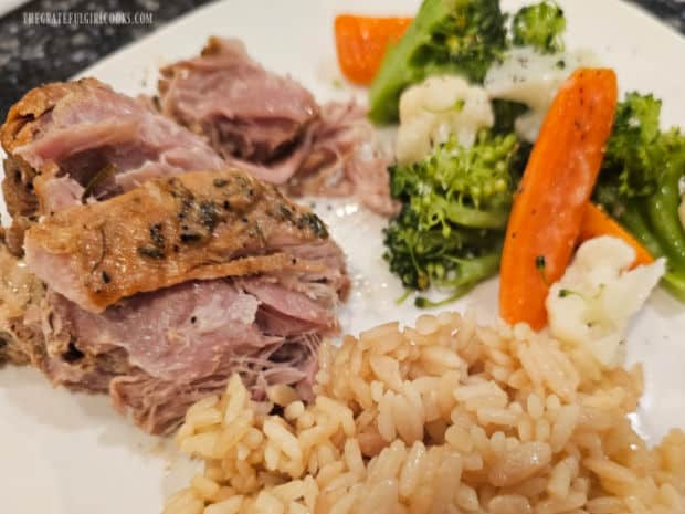 Crockpot Garlic Herb Pork Butt slices served with rice pilaf and veggies on a white plate.