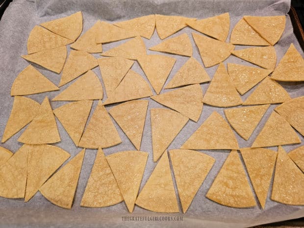 Tortilla wedges are placed on parchment paper in a single layer for baking.