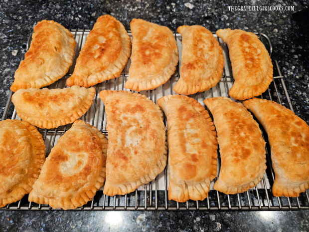 A dozen ground beef empanadas cooling on a wire rack.