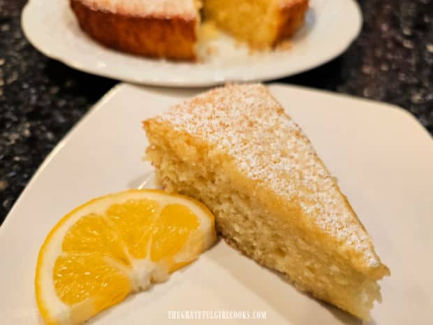 A slice of the lemon olive oil cake with a lemon slice on a white plate.