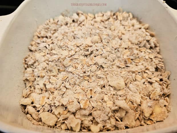 Crumbly topping is evenly sprinkled on top of the fruit until fully covered.