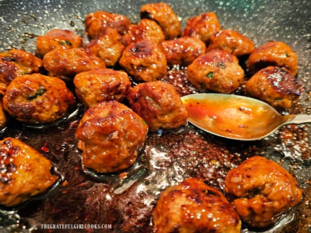 Honey garlic sauce is spooned over the meatballs in the skillet.