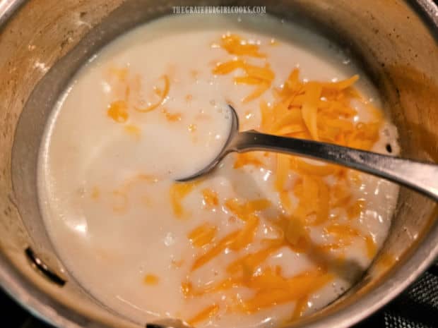 Grated cheddar cheese is added to thickened sauce and stirred to combine.
