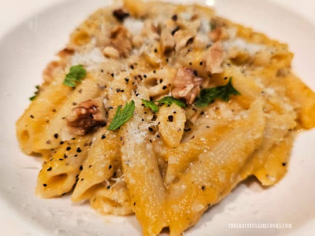 A serving of butternut squash penne pasta in a white bowl.