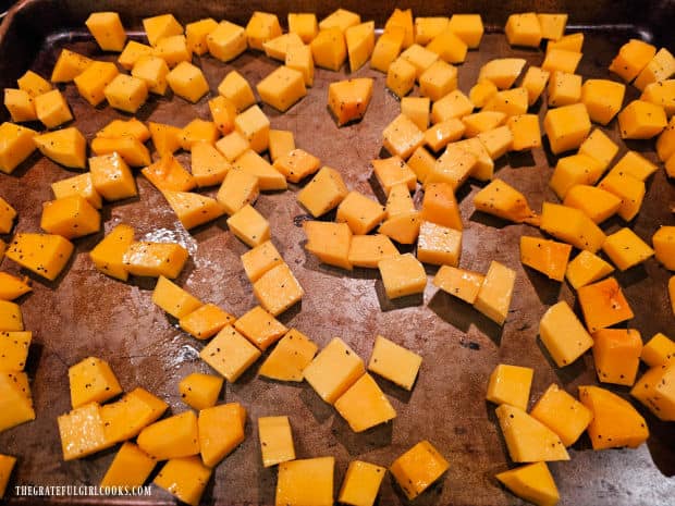 Seasoned butternut squash cubes are spread on baking sheet for roasting.