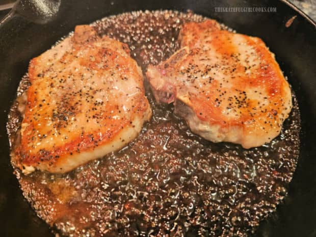 Two pork chops are placed back in the sauce in the skillet.